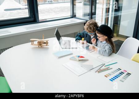 Zwei niedliche kleine Designer, die während der Teamarbeit Online-Daten im Touchpad studieren Stockfoto