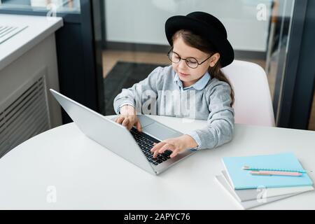 Clevere Casual Schoolgirl in Brillen, die Hausaufgaben vorbereiten und Laptops benutzen Stockfoto