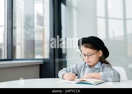 Ernsthafte kleine Schulmädchen in Hut und Brille zeichnen Bild mit Krebse Stockfoto