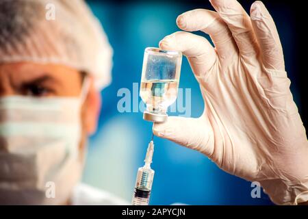 Arzt in medizinischen Handschuhen, der vor der Injektion eine Flasche mit Impfstoff und Spritze hält. Nahaufnahme. Medizin, Wissenschaft und Gesundheitswesen Stockfoto