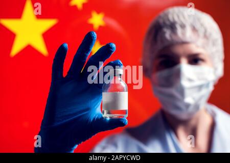Ein Arzt in blauen medizinischen Handschuhen, der eine Flasche mit Impfstoff vor der Flagge Chinas hält. Nahaufnahme. Coronavirus, Epidemie und Gesundheitskonzept Stockfoto