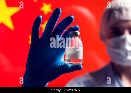 Ein Arzt in blauen medizinischen Handschuhen, der eine Flasche mit Impfstoff vor der Flagge Chinas hält. Nahaufnahme. Coronavirus, Epidemie und Gesundheitskonzept Stockfoto
