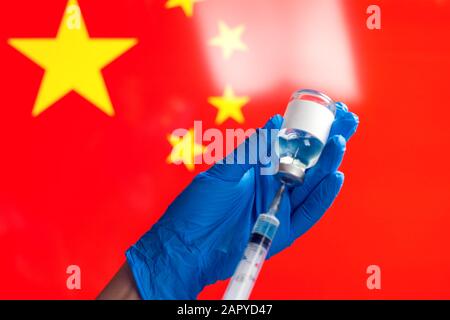 Ein Arzt in blauen medizinischen Handschuhen, der eine Flasche mit Impfstoff und Spritze vor der Flagge Chinas hält. Nahaufnahme. Coronavirus, Epidemie und healthca Stockfoto