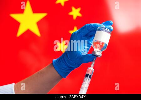 Ein Arzt in blauen medizinischen Handschuhen, der eine Flasche mit Impfstoff und Spritze vor der Flagge Chinas hält. Nahaufnahme. Coronavirus, Epidemie und healthca Stockfoto