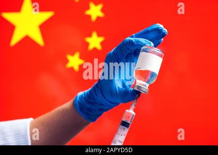 Ein Arzt in blauen medizinischen Handschuhen, der eine Flasche mit Impfstoff und Spritze vor der Flagge Chinas hält. Nahaufnahme. Coronavirus, Epidemie und healthca Stockfoto