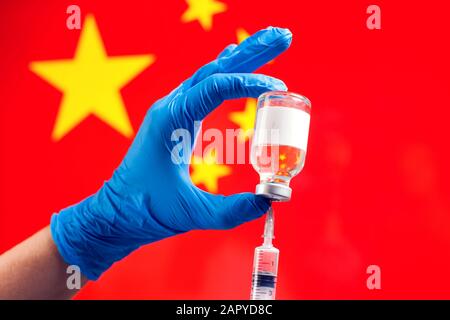 Ein Arzt in blauen medizinischen Handschuhen, der eine Flasche mit Impfstoff und Spritze vor der Flagge Chinas hält. Nahaufnahme. Coronavirus, Epidemie und healthca Stockfoto