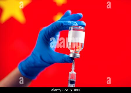 Ein Arzt in blauen medizinischen Handschuhen, der eine Flasche mit Impfstoff und Spritze vor der Flagge Chinas hält. Nahaufnahme. Coronavirus, Epidemie und healthca Stockfoto