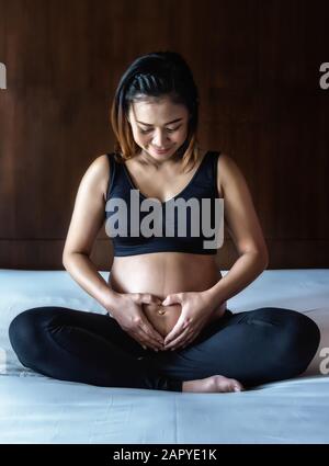 Schwangere Frau, die ihre Hände an ihrem geschwollenen Bauch hält und ein Herz formt Stockfoto