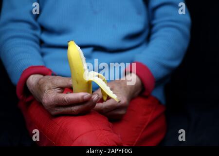 Selektive Fokusaufnahme einer älteren Frau, die einen halb geschälten Mann hält Banane Stockfoto