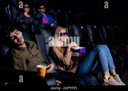 Junger, müder Mann schläft im Kino, während seine Freundin Film im Kino sieht Stockfoto