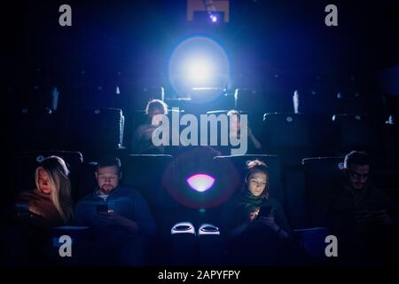 Eine Gruppe mobiler Jugendlicher scrollt im dunklen Kino in ihren Smartphones Stockfoto