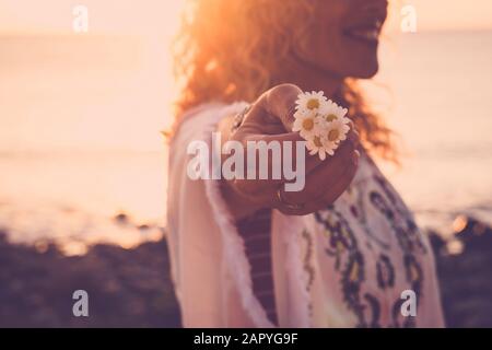 Umwelt und Liebe zum Naturkonzept mit fröhlicher fröhlicher Frau im Hintergrund, die schöne Gänseblümchen mit der Hand hält - Sonne im Hintergrund - Sonnen Stockfoto