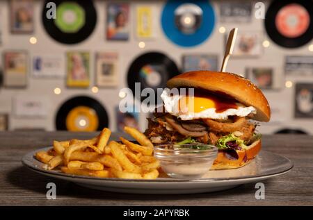 Hausgemachter Schweineburger mit gebratener Eiergrillsauce mit pommes frites auf Holztisch. Isoliertes Bild Stockfoto