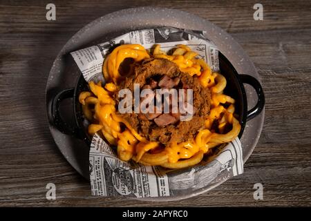 Platte aus gebratenen Kartoffeln mit gekochtem Schweinefleisch und Cheddar-Sauce auf Holztisch. Von oben. Isoliertes Bild Stockfoto