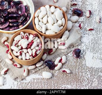 Farbige Bohnen in Holzbechern auf hellem Hintergrund. Stockfoto