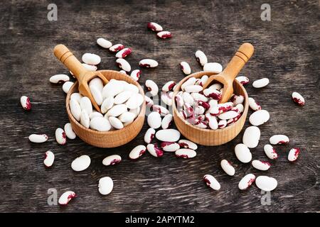 Farbige Bohnen in Holzbechern auf dunklem Woodenhintergrund. Stockfoto