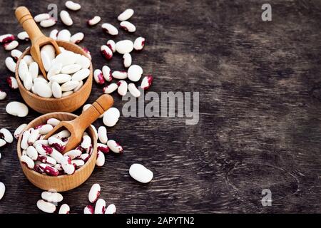 Farbige Bohnen in Holzbechern auf dunklem Woodenhintergrund. Stockfoto
