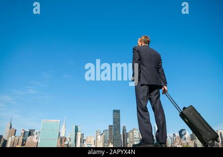 Riesiger, reisender Geschäftsmann, der mit seinem Koffer vor der Skyline der Stadt steht Stockfoto