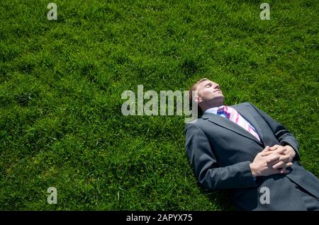 Entspannter Geschäftsmann, der an einem sonnigen Frühlingstag auf einem hellen grünen Rasenplatz liegt Stockfoto