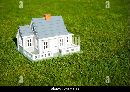Miniaturhaus mit weißem Pickelzaun, das mitten auf einem grünen Rasenplatz steht Stockfoto