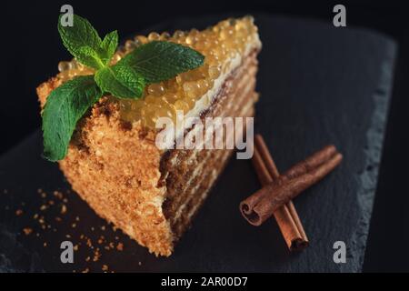 Honig Kuchen mit goldenen Perlen und Minzeblatt und Zimt auf Steinplatte auf schwarzem Hintergrund Stockfoto