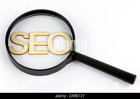 SEO Holz Buchstaben für Search Engineoptimierung unter einem schwarzen Lupe auf einem isolierten weißen Hintergrund Stockfoto