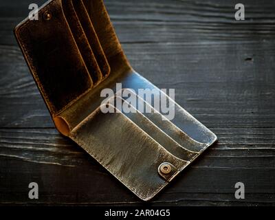 Handgefertigtes Kunsthandwerk aus Leder braun leeres Portemonnaie auf schwarzem Holzhintergrund. Finanzen, Armut, Geldkonzept Stockfoto