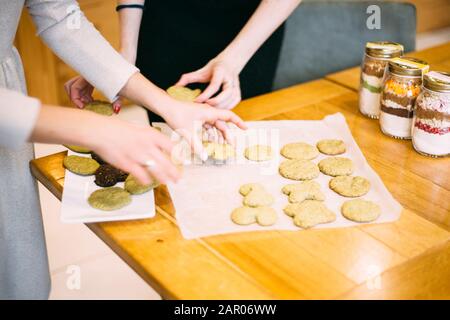 Die Hände der Frauen bereiten Teller verschiedener Art von Plätzchen auf Holztisch vor. Stockfoto