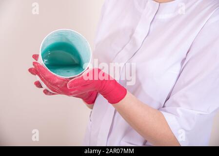 Meister in roten medizinischen Handschuhen hält blaue flüssige Paste für die Zuckerenthaarung Stockfoto