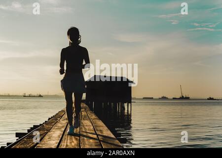 Silhouette der Frau, die morgens auf einer Holzbrücke bei Sonnenaufgang joggt. Stockfoto