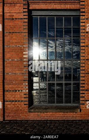 Fenster in Ziegelwand mit Spiegelung des Hamburger Containerhafens und Wolken und sonnenstern am Himmel Stockfoto