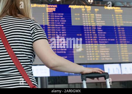 Frau schaut auf die Anzeigetafel am Flughafen. Wählen Sie ein Land für Reisen oder Migration aus. Stockfoto