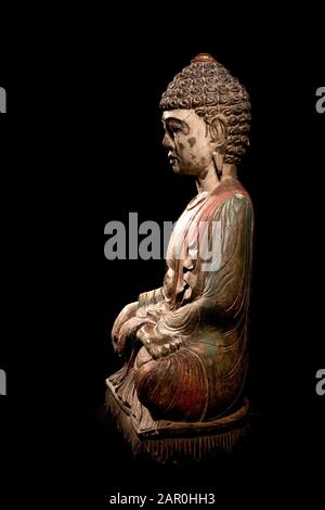 Farbenfrohe, bemalte Buddha-Statue, die in lotus-position sitzt und innere Ruhe vor schwarzem Hintergrund bietet Stockfoto