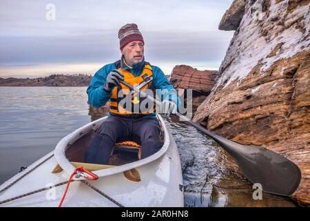 Männer, die eine Lebensjacke tragen, Neopren-Handschuhe und Woll-Mütze paddeln das Expeditionskanu entlang der Eisfelsen aus Sandstein, die Landschaft der kalten Jahreszeit auf Horset Stockfoto