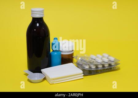 Gewebe, Nasentropfen, Thermometer, Hustensirup, Spray, Pillen und Blister auf gelbem Hintergrund. Stockfoto