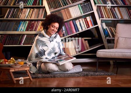 Frau in Hausbibliothek auf dem Boden sitzend und im Buch schauend Stockfoto