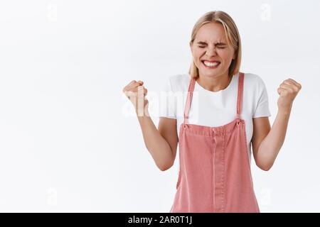 Erleichtert, glücklich gut aussehende junge kaukasische Frau erreicht endlich das Ziel, jubelt mit der Faust und sagt Ja, schmunzelnd zufrieden, triumphierend Stockfoto