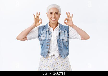 Selbstbewusste, sorglose alte Frau hat kein Problem, sich einen modernen, stilvollen Look zu suchen, der okay, eine gute Geste zeigt und lächelnd zufrieden, zufrieden mit gutem Ergebnis, geben Stockfoto