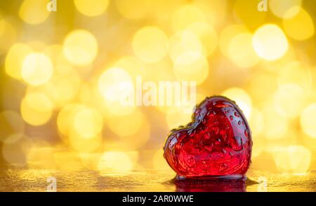 Rotes transparentes Herz in Wassertropfen auf goldenem Grund mit Bokeh. Liebeshintergrund. Valentinstag Stockfoto