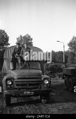 STUPINO, REGION MOSKAU, RUSSLAND - CIRCA 1992: Das Porträt zweier Soldaten der russischen Armee, die auf dem Kabinendach eines Lastwagens ZIL-130 sitzen. Schwarz und Weiß. Filmscan. Große Körnung. Stockfoto
