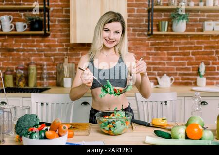 Lächelnde junge Hausfrau mischt frischen Salat. Gesunder Lebensstil Und Essen. Ernährung. Diät-Konzept. Gesunde Ernährung. Wohlbefinden, Wellness. Stockfoto