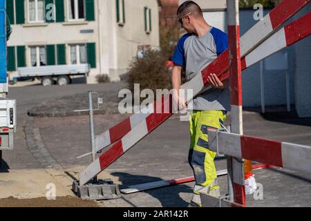 Der junge Bauarbeiter hält Barrieren eines Bauwerks in seinen Händen. Straßenbesen; wegräumen; Besen für Straßenbau; Schrubber; Vehi Stockfoto