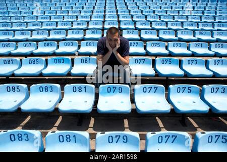 Der traurige hispanische 35-jährige Mann sitzt allein auf einem riesigen Stand leerer Plätze in einem Fußballstadion, dessen Kopf sich am Ende der Saison in den Händen befindet Stockfoto
