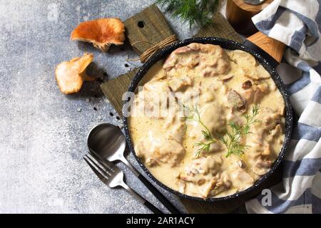 Fricasse - Französische Küche. Huhn in einer cremigen Soße mit Pilzen in einer Pfanne auf hellem Steingrund gehütet. Kopierbereich. Stockfoto