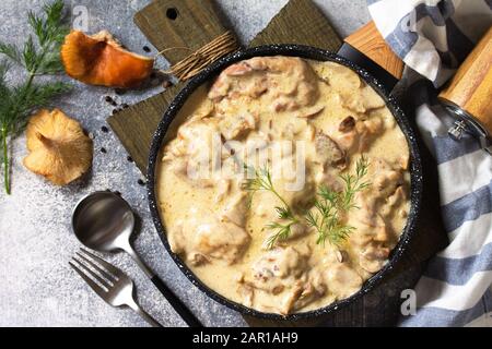 Fricasse - Französische Küche. Huhn in einer cremigen Soße mit Pilzen in einer Pfanne auf hellem Steingrund gehütet. Draufsicht mit Kopierbereich. Draufsicht auf Stockfoto