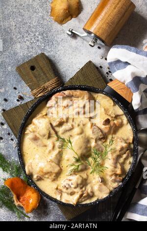 Fricasse - Französische Küche. Huhn in einer cremigen Soße mit Pilzen in einer Pfanne auf hellem Steingrund gehütet. Draufsicht mit Kopierbereich. Draufsicht BA Stockfoto