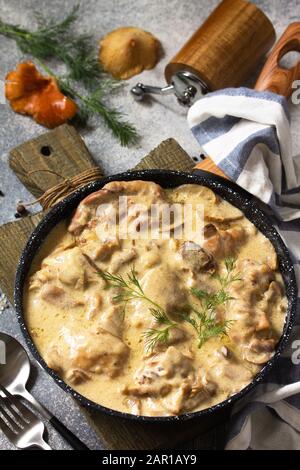 Fricasse - Französische Küche. Huhn in einer cremigen Soße mit Pilzen in einer Pfanne auf hellem Steingrund gehütet. Stockfoto