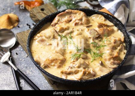 Fricasse - Französische Küche. Huhn in einer cremigen Soße mit Pilzen in einer Pfanne auf hellem Steingrund gehütet. Stockfoto