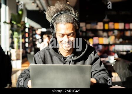 Der junge Afroamerikaner steht in Verbindung mit einem Videoanruf, der junge lateinamerikaner schaut Multimedia-Inhalte an, er surft im Internet und sucht nach neuem Blos Stockfoto