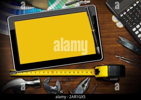 Konzept Zur Verbesserung der Wohnqualität. Digitales Tablett mit leerem gelbem Bildschirm auf einer Holz-Werkbank mit Heimwerkerwerkzeugen und einem Taschenrechner mit Euro-Währung. Stockfoto